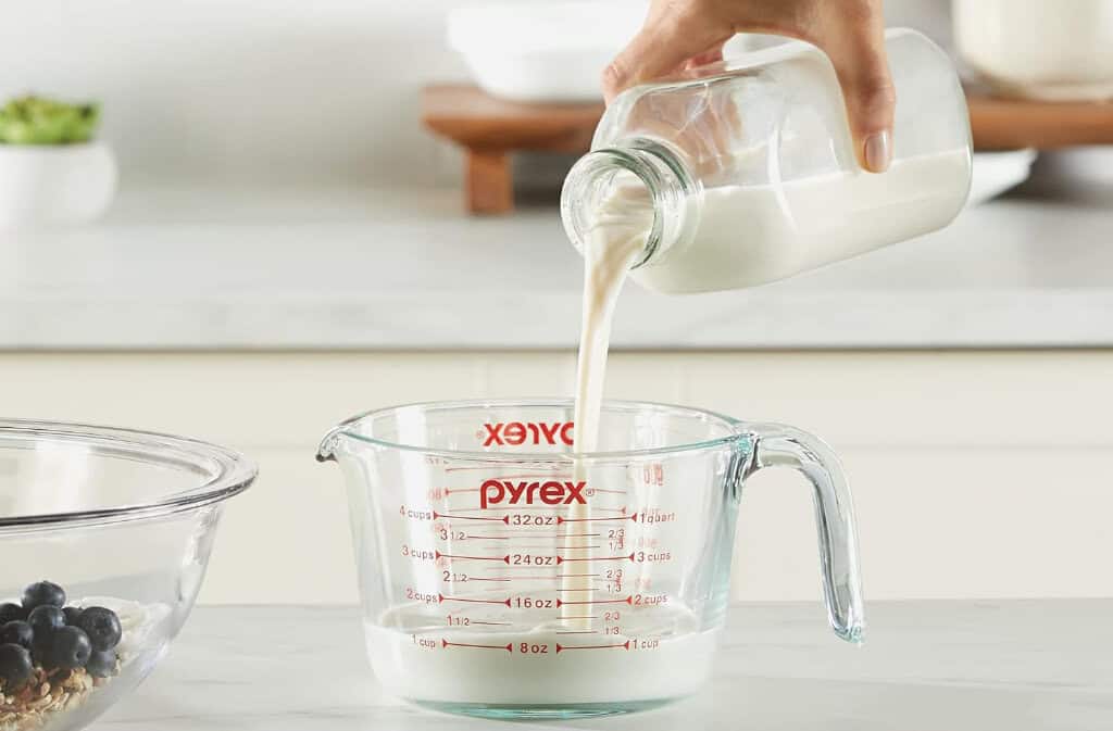 Pouring milk into a measuring cup in kitchen.