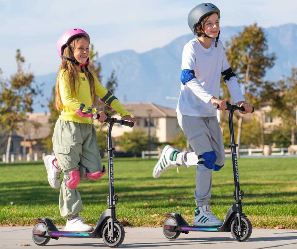 Children riding scooters outdoors with helmets.