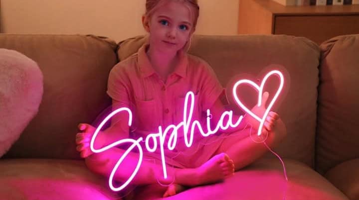 Child with pink neon sign, "Sophia" and heart.