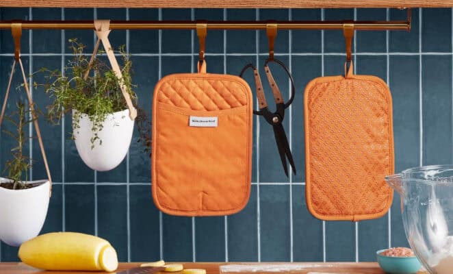 Orange oven mitts hanging in kitchen scene.