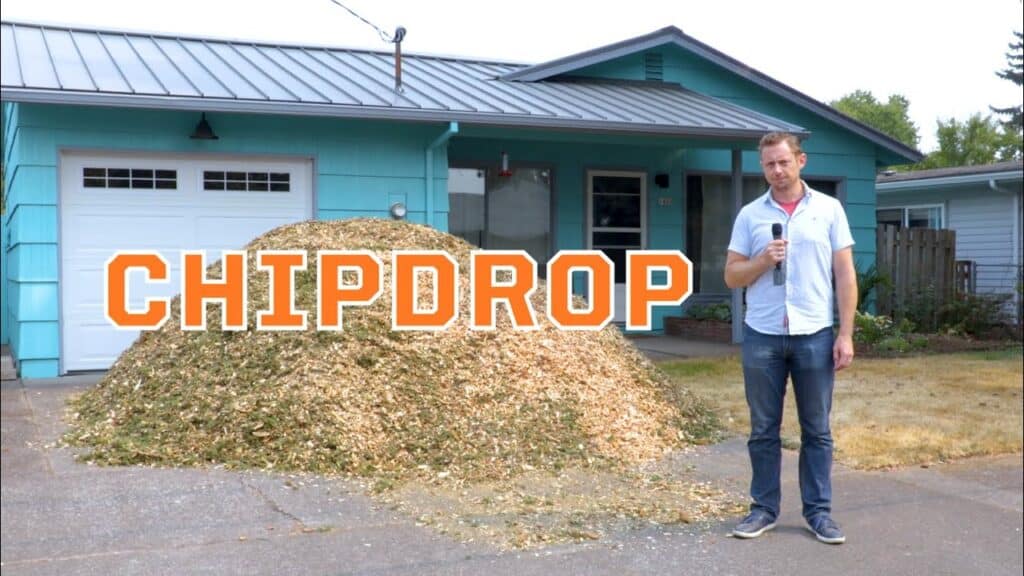 Man standing by wood chip pile in driveway.