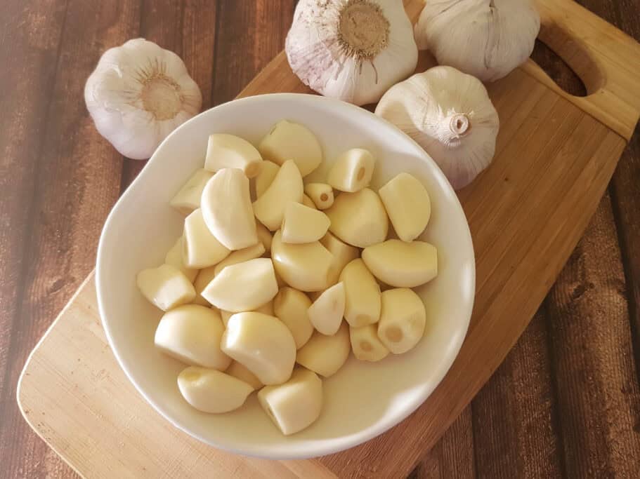 Garlic cloves peeled in white bowl on wooden board.