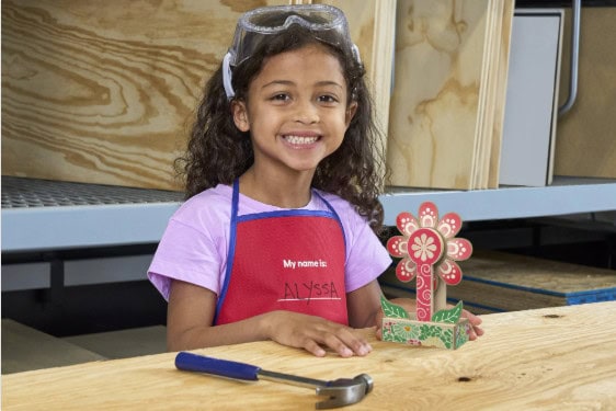 Child with craft flower, smiling in workshop.