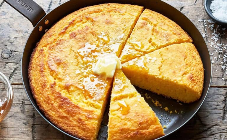 Sliced cornbread with butter and honey in skillet.