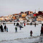Families enjoying ice skating on a frozen pond in Nuuk, surrounded by traditional Greenlandic architecture.