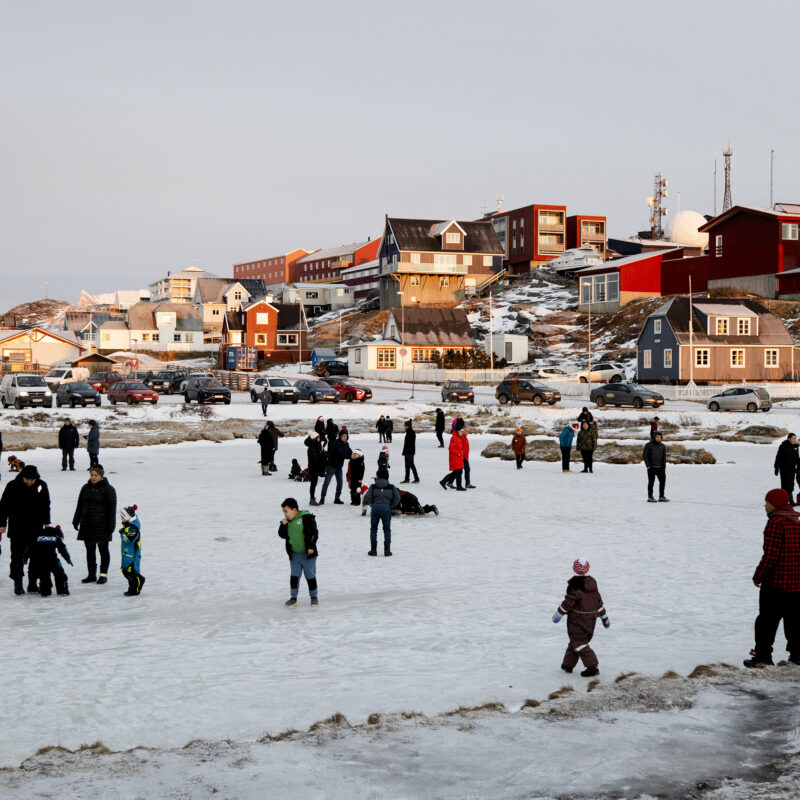 Families enjoying ice skating on a frozen pond in Nuuk, surrounded by traditional Greenlandic architecture.