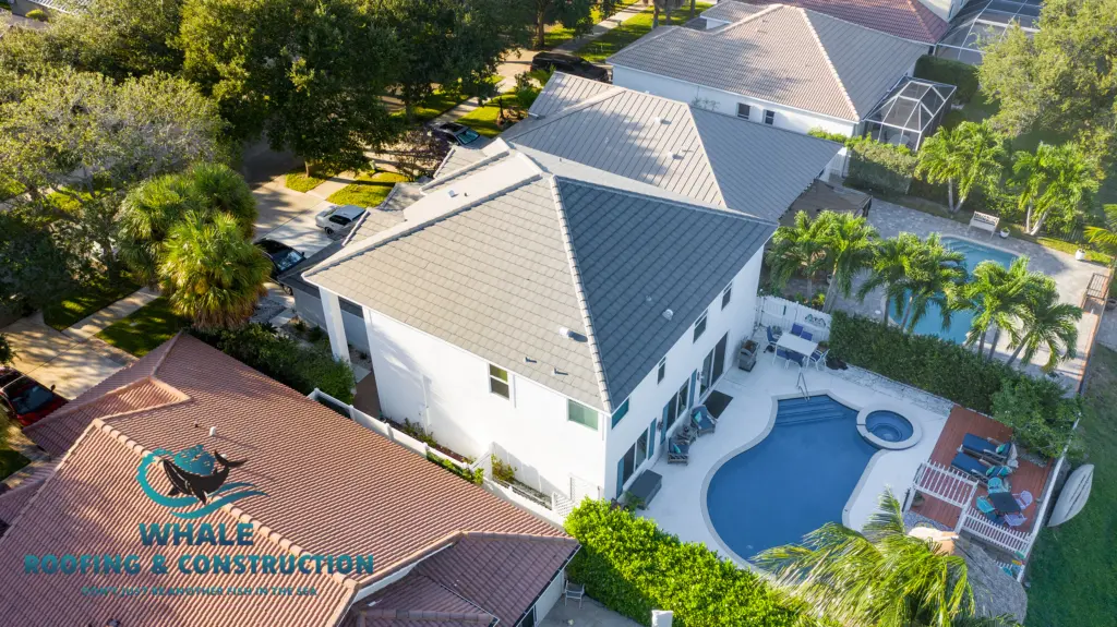 Aerial view of a house with a gray tile roof, backyard pool, and patio, surrounded by neighboring homes and trees. Whale Roofing & Construction logo in the bottom left corner.