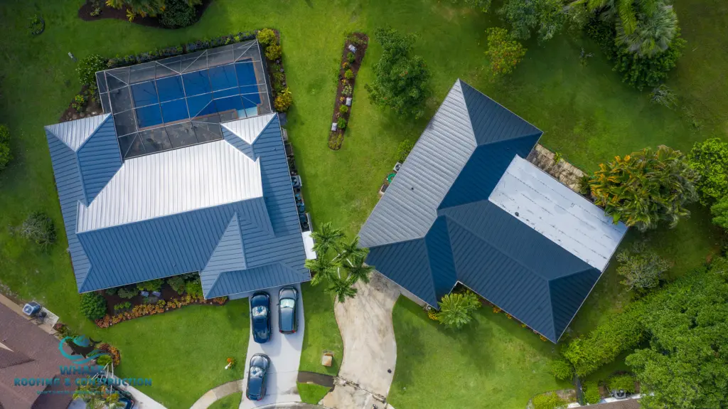 Aerial view of two houses with metal roofs, driveways, and green lawns; cars are parked outside, and one house has a screened pool area.