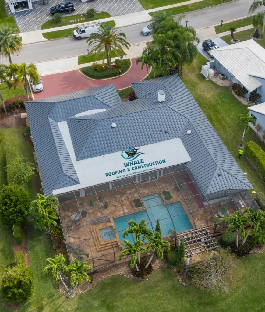 Metal Roof Replacement in Parkland 2 Aerial view of a house with a screened-in pool enclosure and a gray metal roof displaying a "Whale Roofing & Construction" sign. Landscaping surrounds the property.