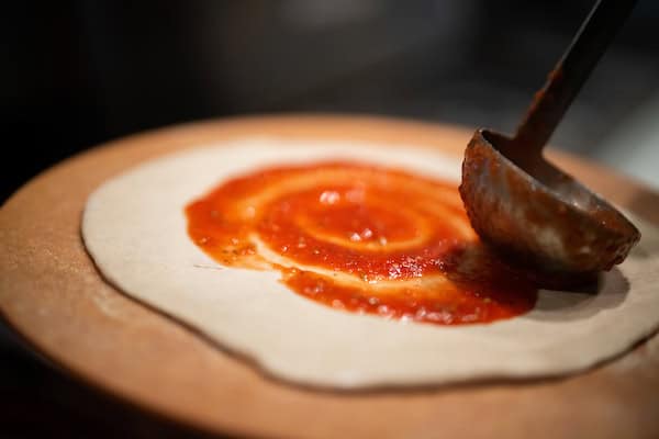 Chef preparing wood-fired pizza dough with sauce before putting into the Stone Hearth Oven at Mama DeVechio's Pizzeria