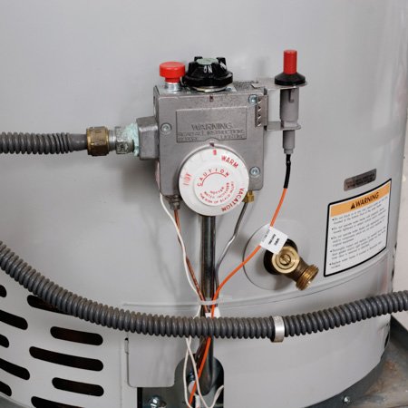 Close-up of a water heater control panel with a temperature dial, emergency red button, and attached wires, ready for repair.