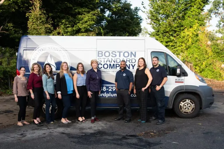 A group of nine people stands confidently in front of a company van labeled "Boston Standard Company," parked on a tree-lined street, ready to assist with any inquiry or service. Don't hesitate to contact them for all your needs.