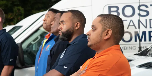 Four men in branded work shirts stand proudly in front of vans adorned with business logos, ready to tackle any job, from basic repairs to circuit breaker installation.