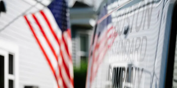 An American flag flutters near a building, with the text "Boston Standard Company" reflecting on a surface. Known for expert plumbing installations and reliable service, this company stands as a beacon of quality craftsmanship in the industry.