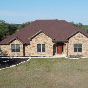 Front view of a single-story, light-brown stone house with a dark reddish-brown metal roof in San Antonio, TX