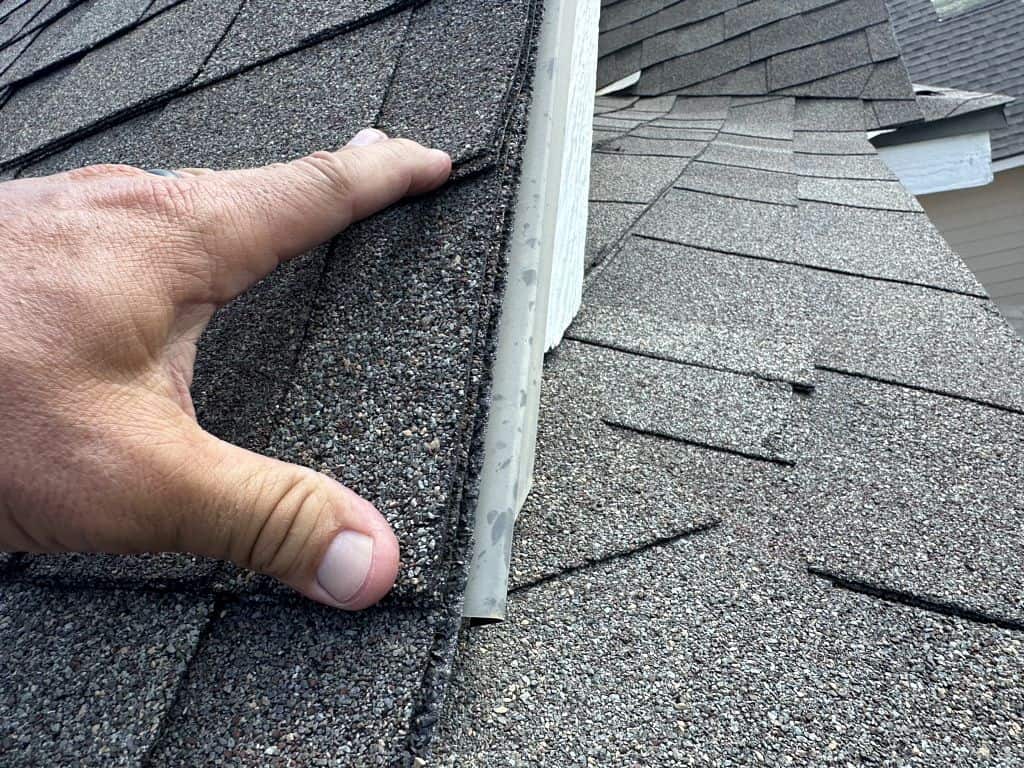 Contractor lifting asphalt shingles to inspect roof flashing during an estimate evaluation