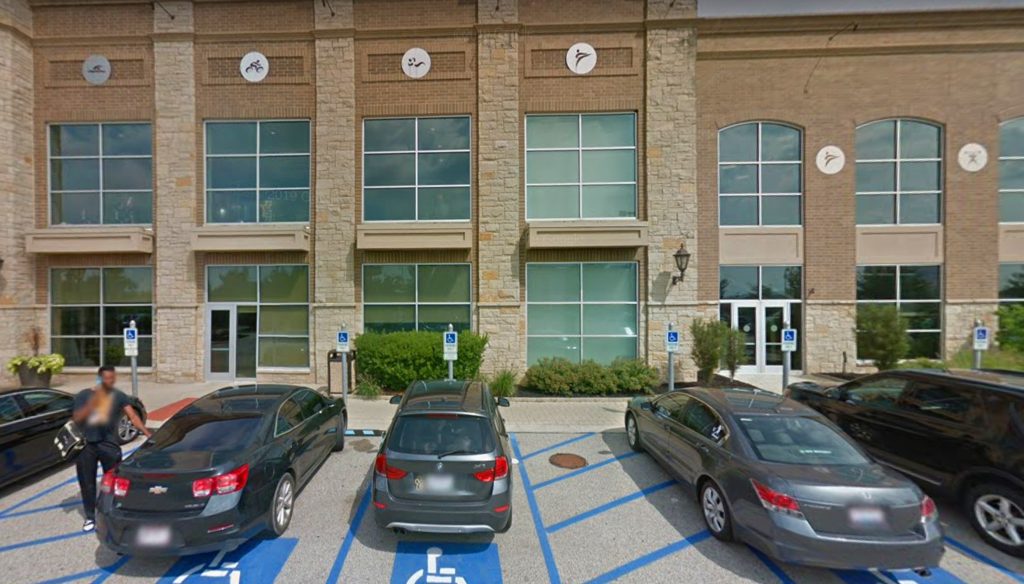 A building with large windows and stone accents, viewed from a parking lot freshly paved by an asphalt contractor. Several cars are parked in accessible spaces out front, with accessibility signs visible and a person walking nearby.