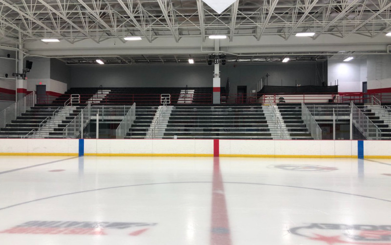 View of empty bleachers in an indoor ice hockey rink, with red, blue, and yellow lines on the ice and a white ceiling with exposed beams above—similar precision found in a top Asphalt Paving Company’s work.