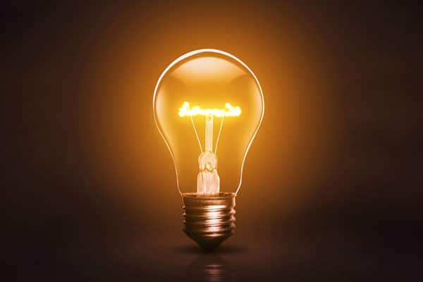 A glowing incandescent light bulb with a visible filament, set against a dark background.