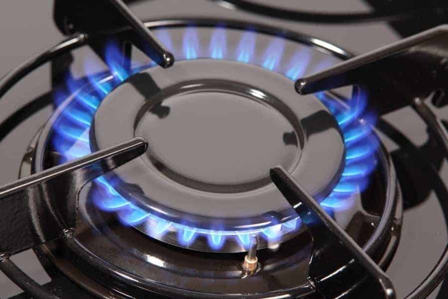 A lit gas stove burner with a blue flame is shown, surrounded by a metal grate, highlighting the absence of common pilot light issues.