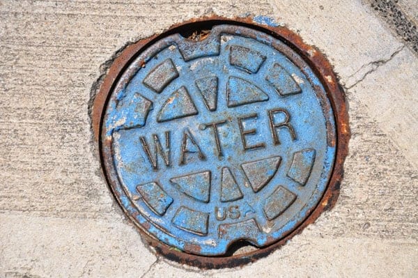 Blue round water utility cover on concrete pavement.
