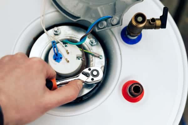 A person uses a wrench to adjust components on top of a water heater.
