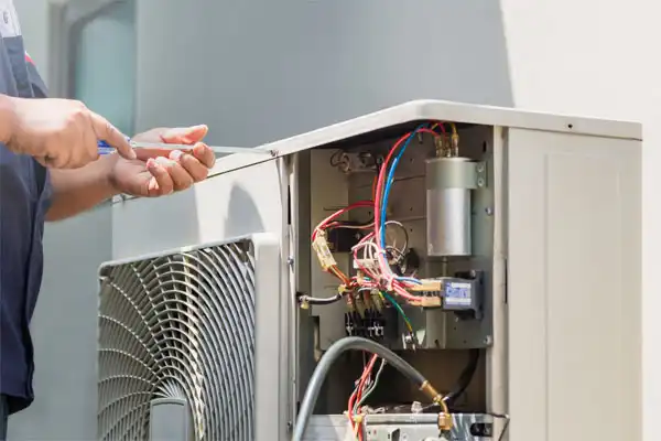 Person repairing an outdoor air conditioning unit, using a tool to work on exposed wiring and components.