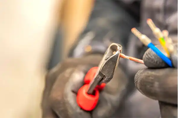 Gloved hands deftly use red-handled pliers to cut the end of a copper wire, while other colored wires rest securely in the other hand, highlighting the precision required in electrical installation.