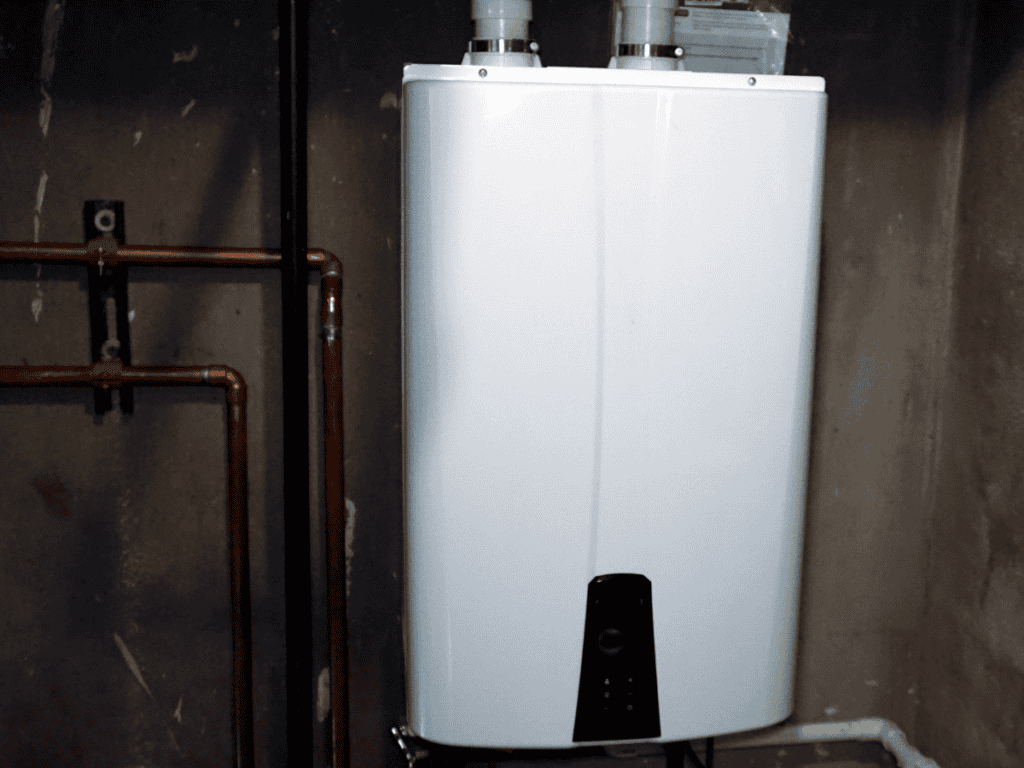 White tankless water heater mounted on a concrete wall, with copper pipes connected to it.