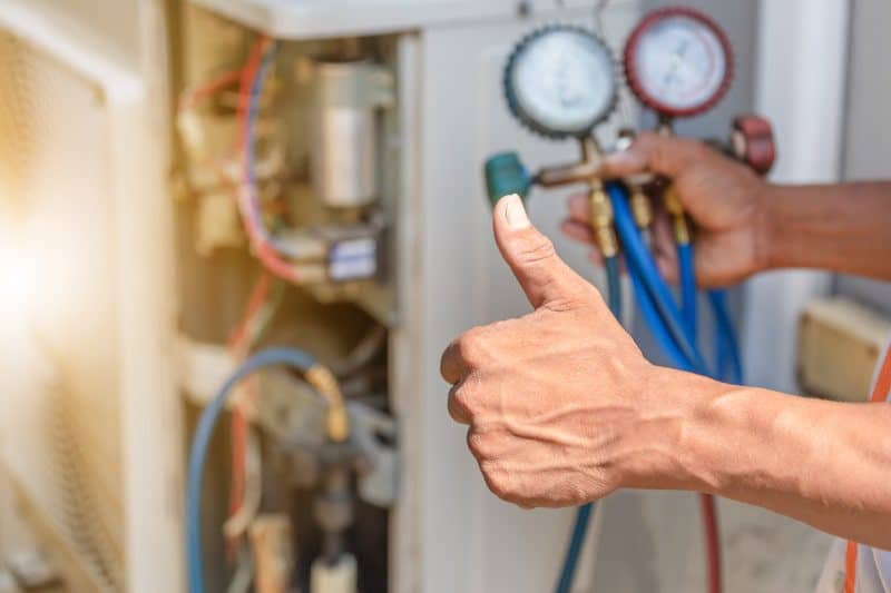 Person giving thumbs up while checking HVAC system with pressure gauges.
