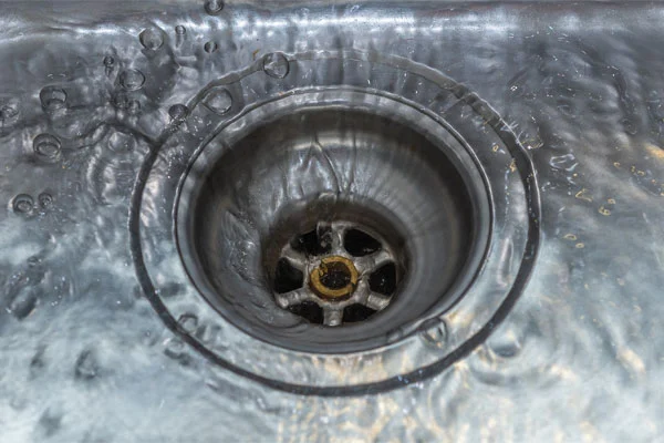 Close-up view of water flowing into a metal sink drain, showing the circular pattern and wet surface around it.
