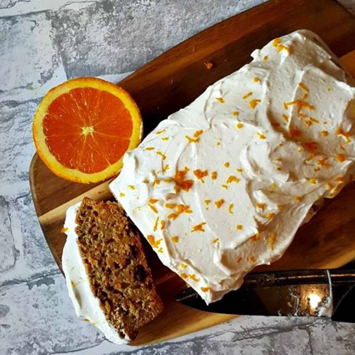 carrot cake with a slice cut showing knife and half an orange