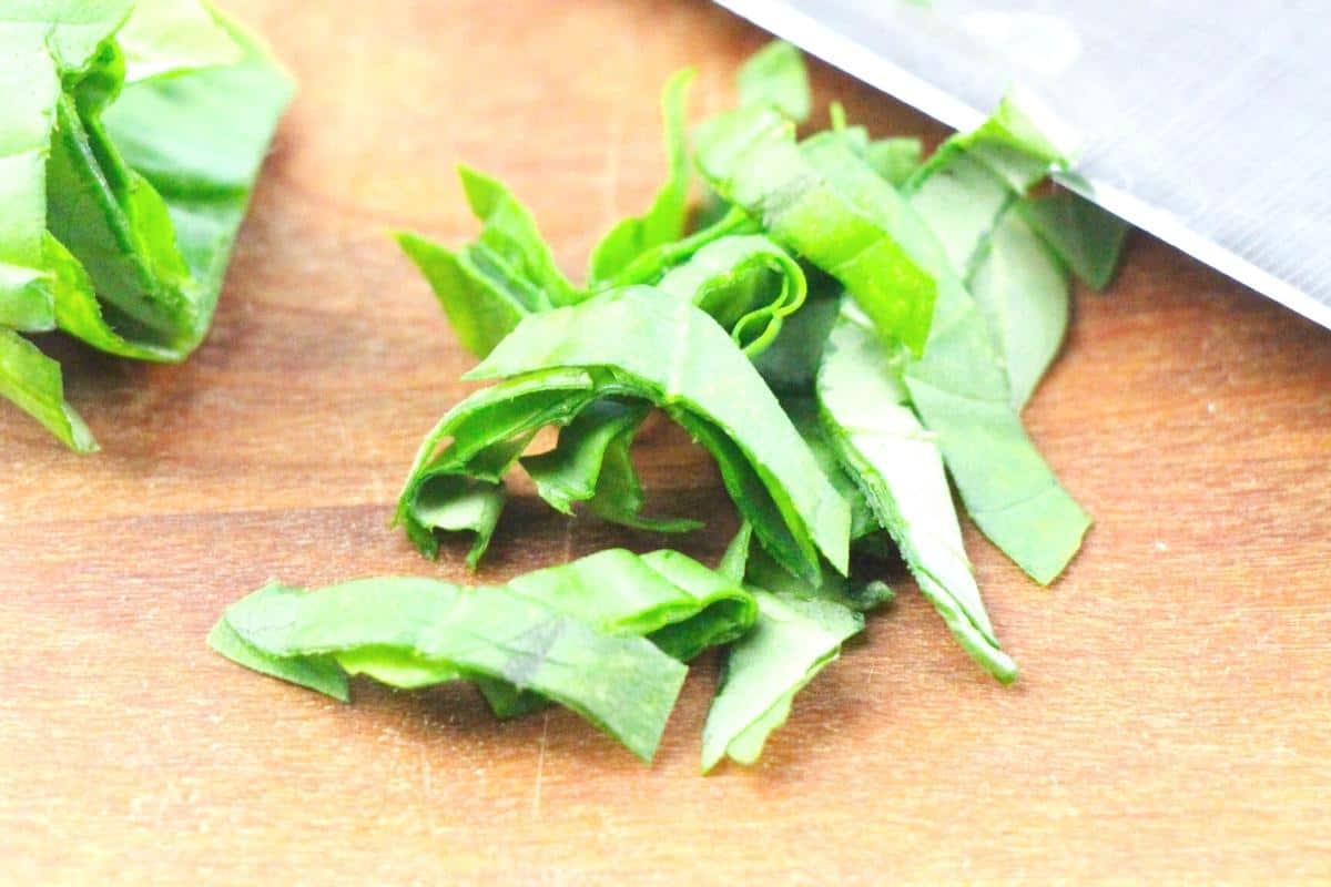 chopping basil on a wooden board with a sharp knife