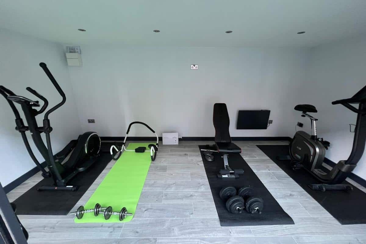 home gym in a garden room with mats on the floor and a cross trainer, an exercise bike and weights.