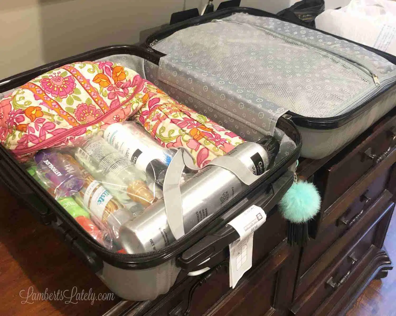 suitcase packed with pink floral toiletry bags and plastic bags for bottles.