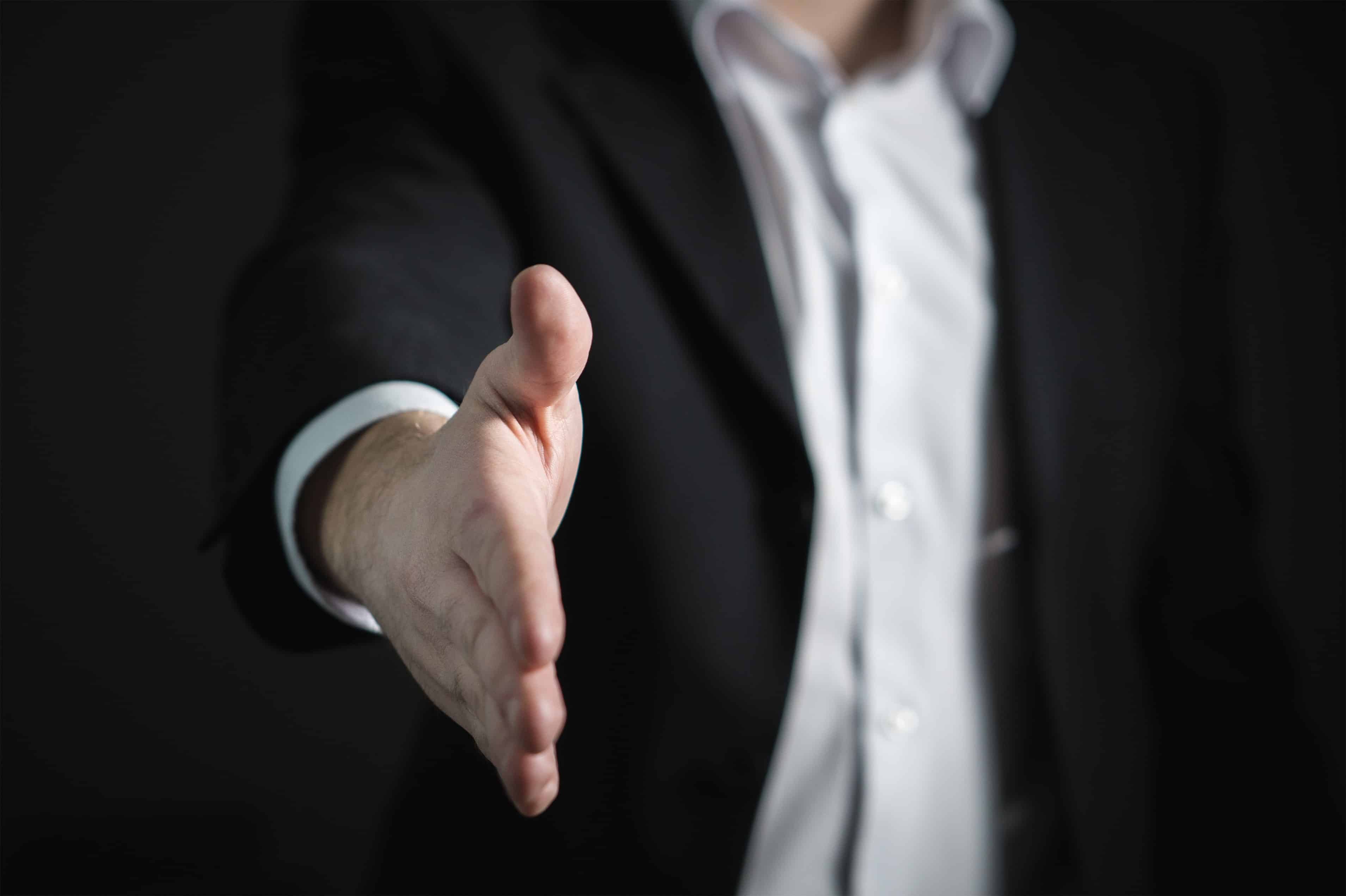 A man in black suit extending a handshake