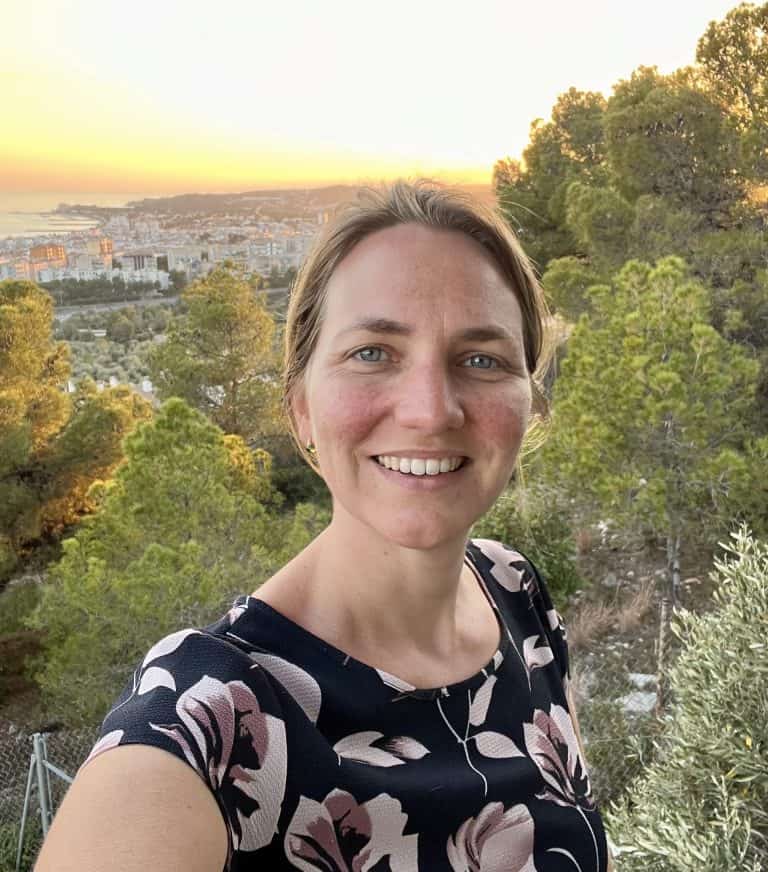 selfy picture of a woman standing in front of a sunset.