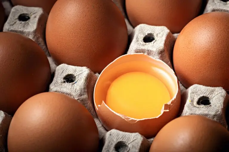 Close-up of brown eggs in a cardboard egg carton, with one egg cracked open to reveal the yolk.