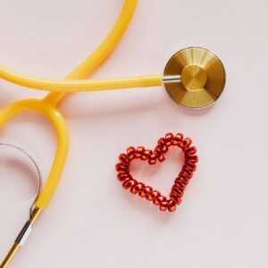 A yellow stethoscope and a red beaded heart on a soft pink background, symbolizing heart health, menopause, and the importance of cardiovascular care for women.