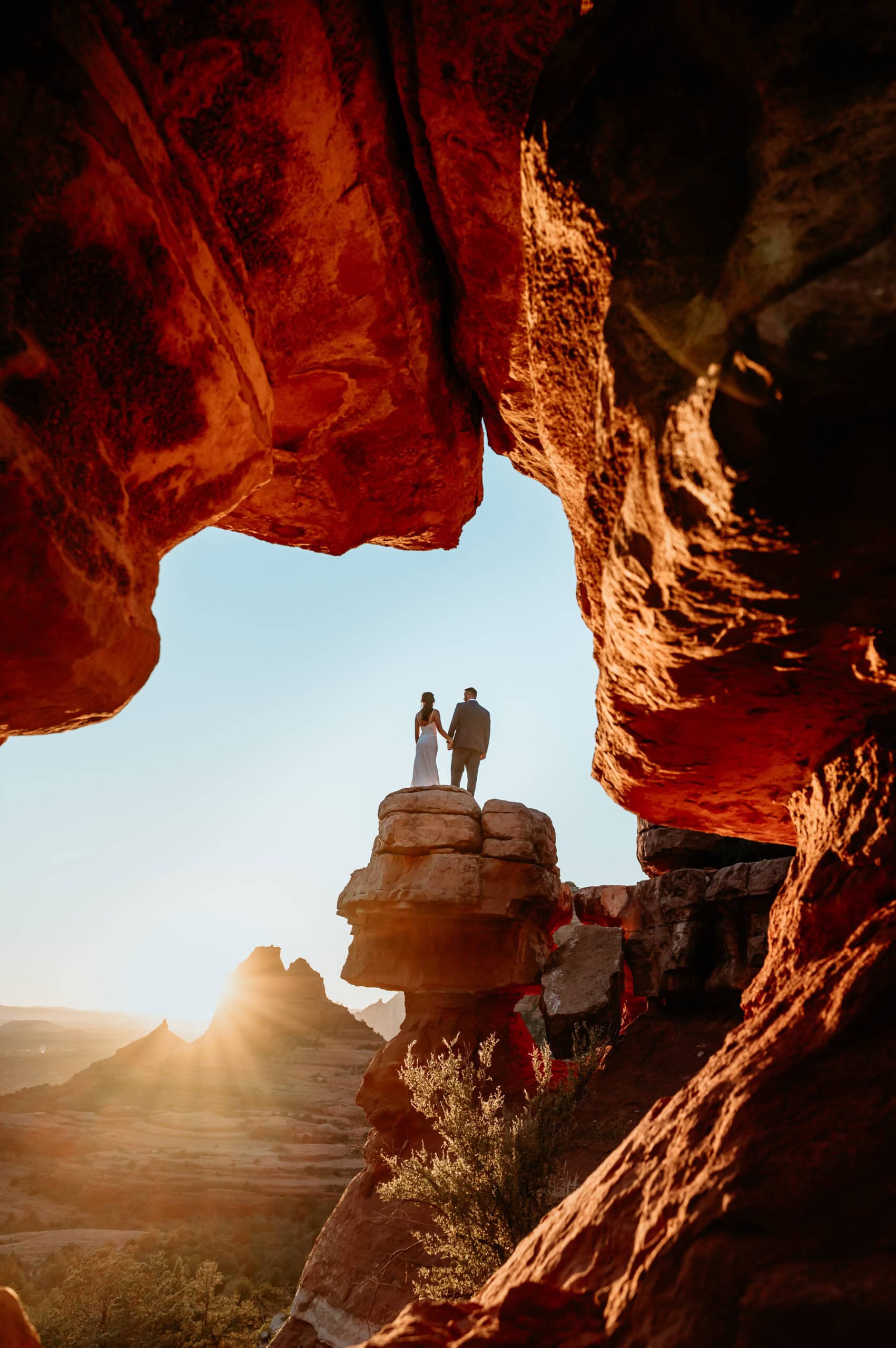 Couple standing on a pedestal framed by red rocks during their Sedona Elopement in Arizona