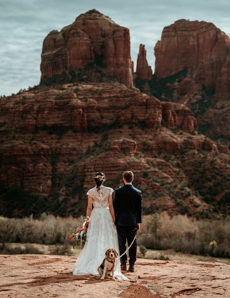 couple looking out at Cathedral Rock with their pup behind them during their Arizona elopement in Sedona by Stratus Adventure Photography