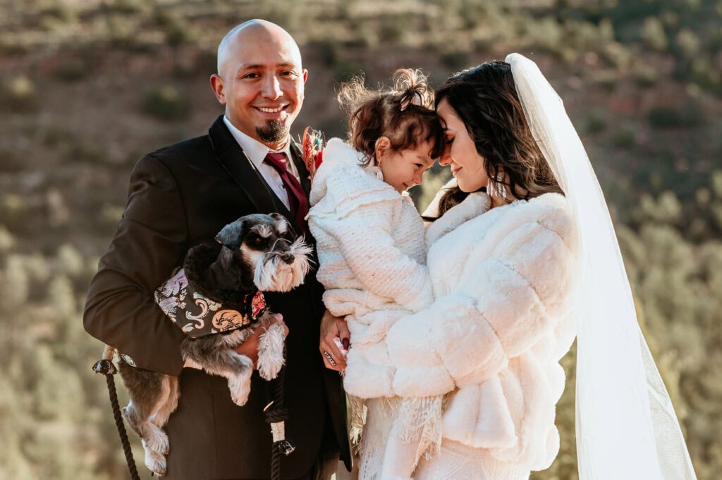 groom holding dog smiles as bride and little girl nuzzle during their elopement with family