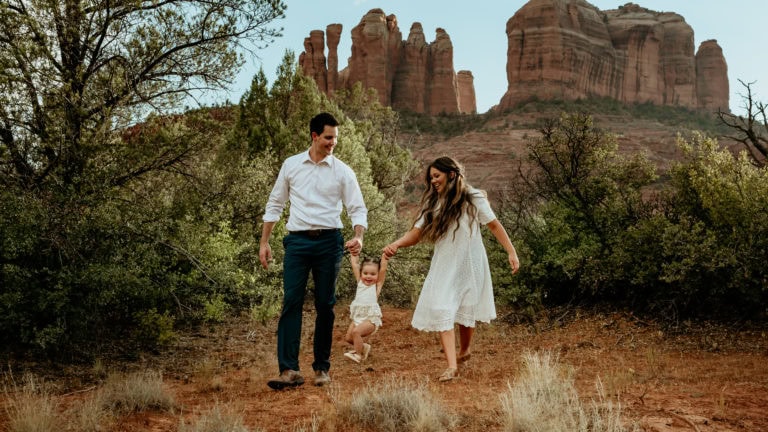 Couple walks and swings their little girl with Cathedral Rock in the background