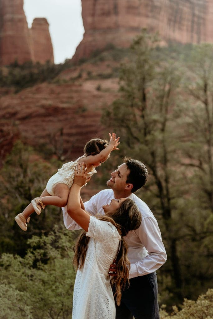 Mom and Dad hold their little girl up in the air at the base of Cathedral Rock in Sedona
