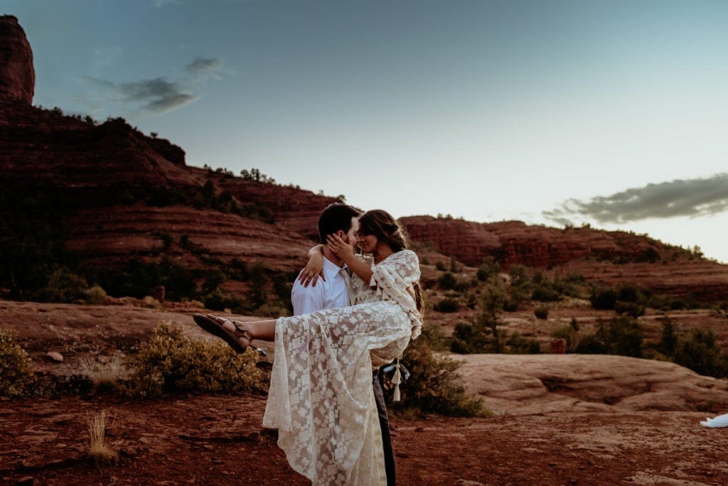 Husband holds and spins wife as the very last of the sunlight dips behind the red rocks of Cathedral Rock