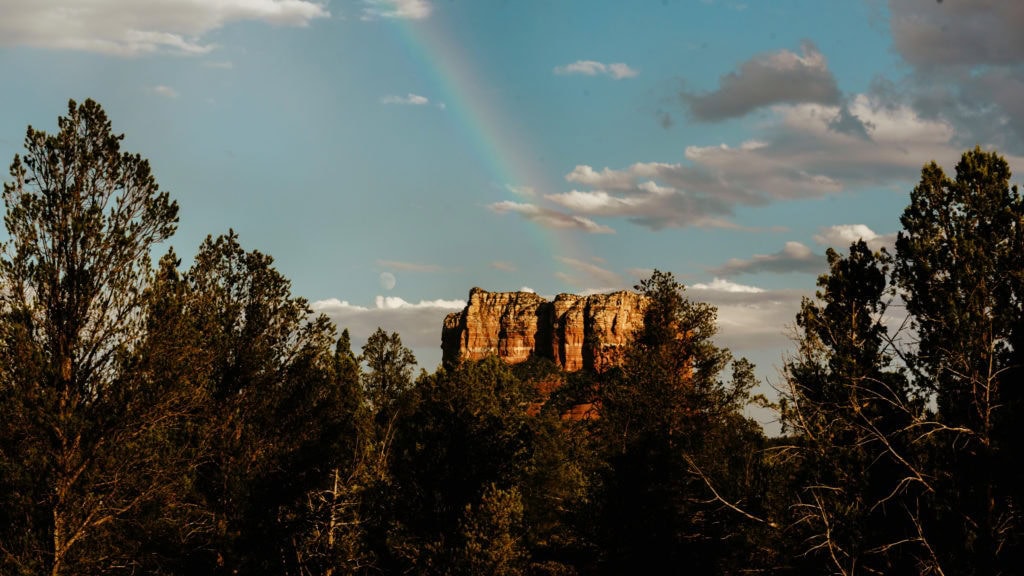 Rainbow perfectly placed after a brief rain over Capitol Butte Rock with moon rising in the distance