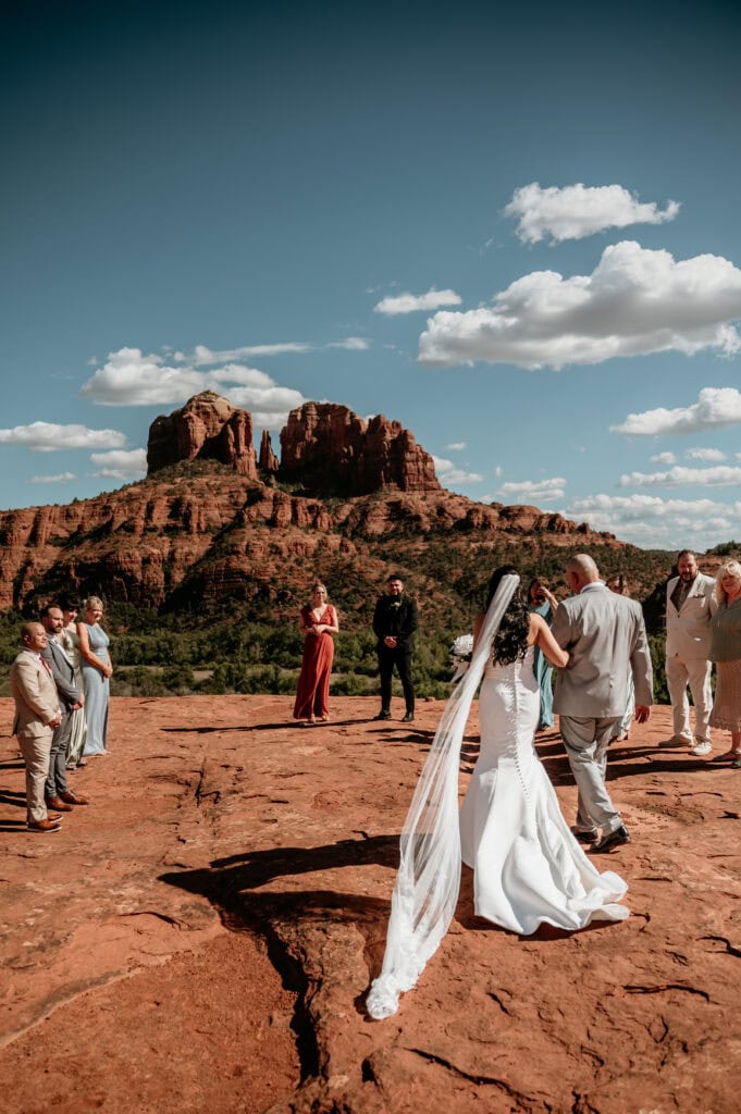 father of the bride walks her down a makeshift isle out in nature during their Sedona elopement wedding