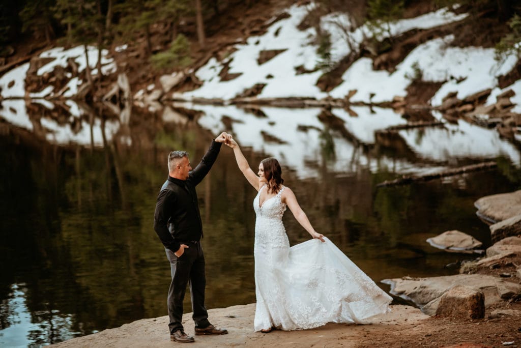 Groom spins his bride as they dance at the edge of a lake