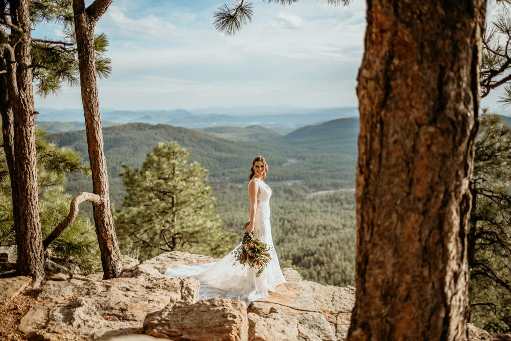 Breathtaking views of trees rolling in the distance as bride stands on ledge of the Mogollon Rim