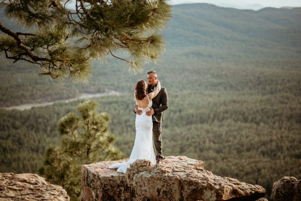 Evergreen as far as the eye can see as an elopement couple stand at the edge of the Mogollon Rim